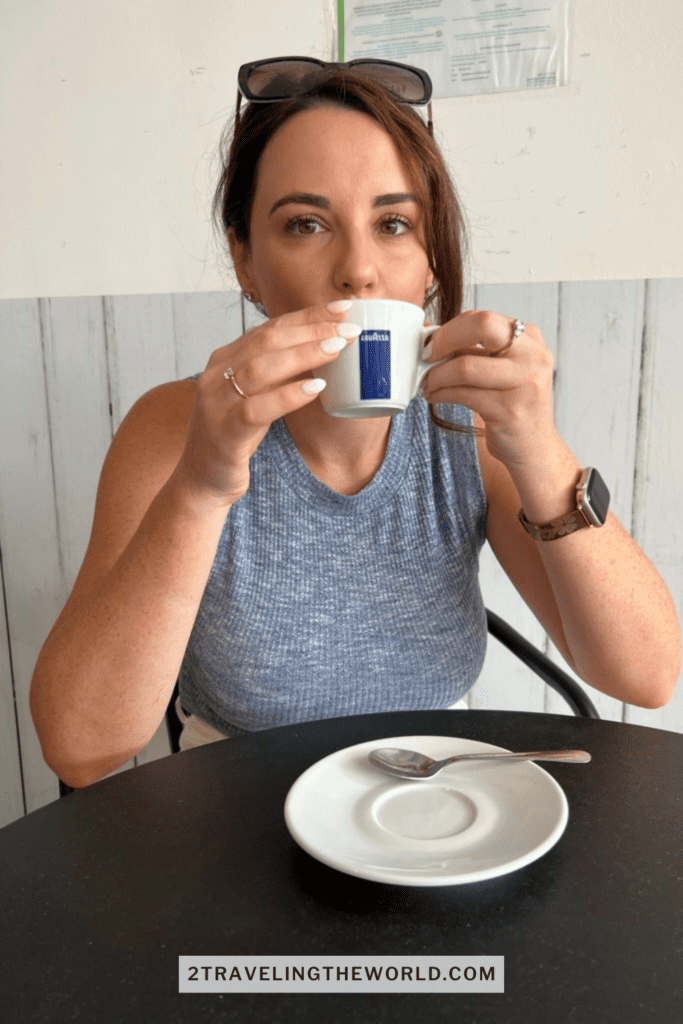 woman sitting an espresso drink in a coffee shop in central algarve. She is wearing a blue shirt and holding a small cup up to her mouth.