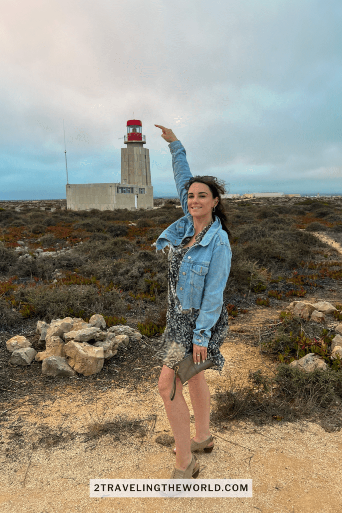 Portugal travel guide: Girl standing in front of the Sagres Lighhouse poinint to the tip of lighthouse. Beautiful place to watch the sun set along the beautiful Algarve Coast