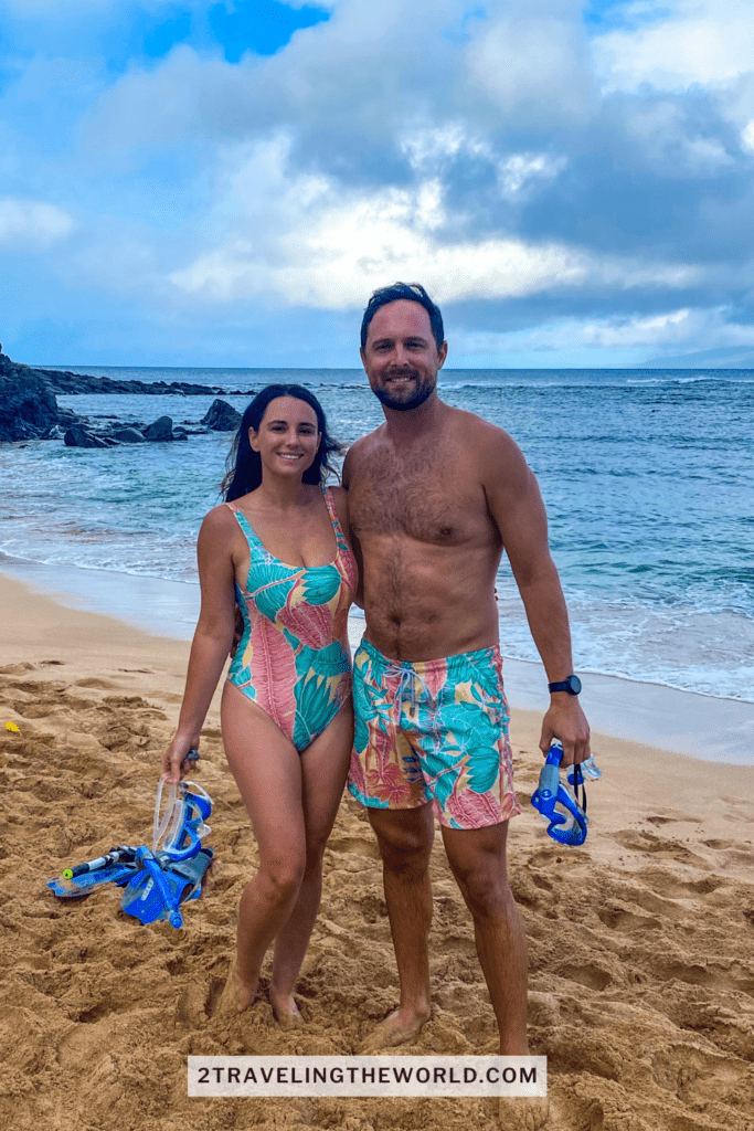 maluaka beach. This image shows Jordyn and Michael from 2 traveling the world blog standing in matching bathing suits. They are holding snorkel equipment before they jump in to swim with turtles at turtle town beach maui.