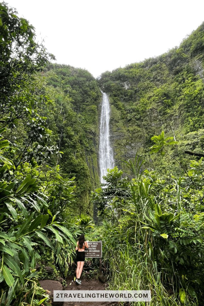 Waimoku Falls waterfall in Maui hawaii. A woman is looking up at the waterfall.