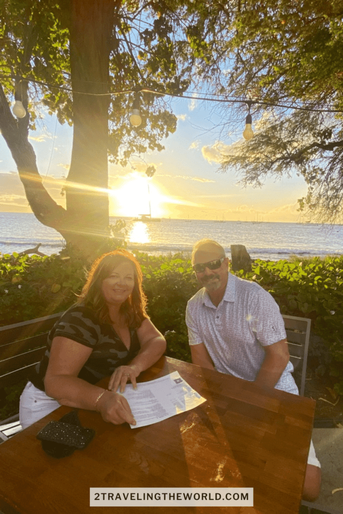 a man and a woman sitting at star noodle restaurant in Maui. The sun is setting on the ocean behind them.