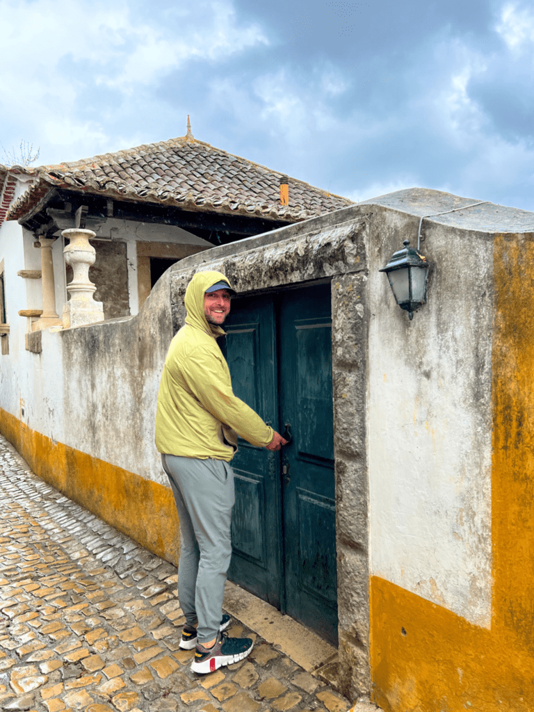 man standing next to a small European door druing portugal trip to Obidos in central portugal