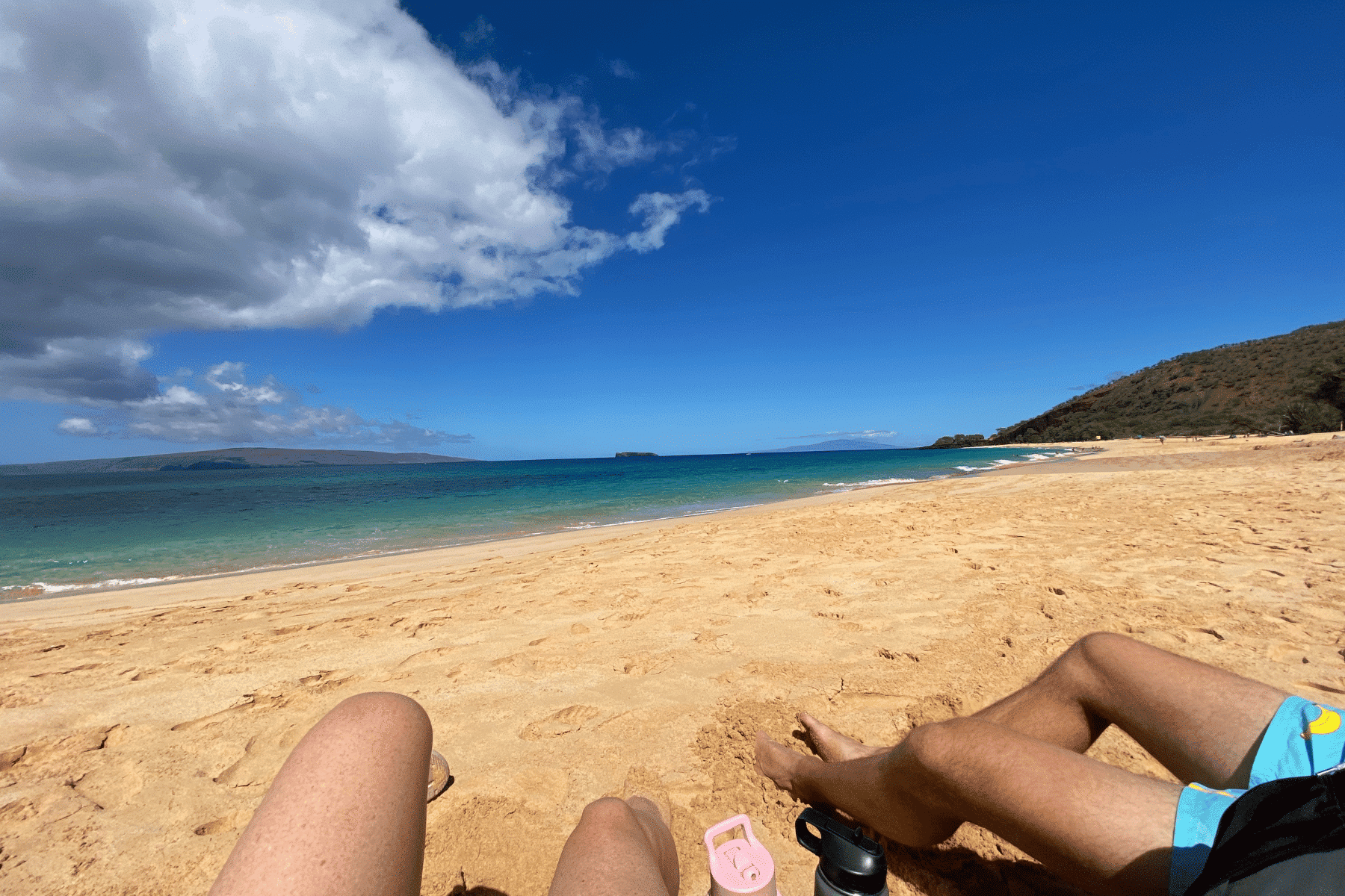 where to stay on maui - couple sitting on south Maui beach. Bright blue ocean in the background and white sand beach