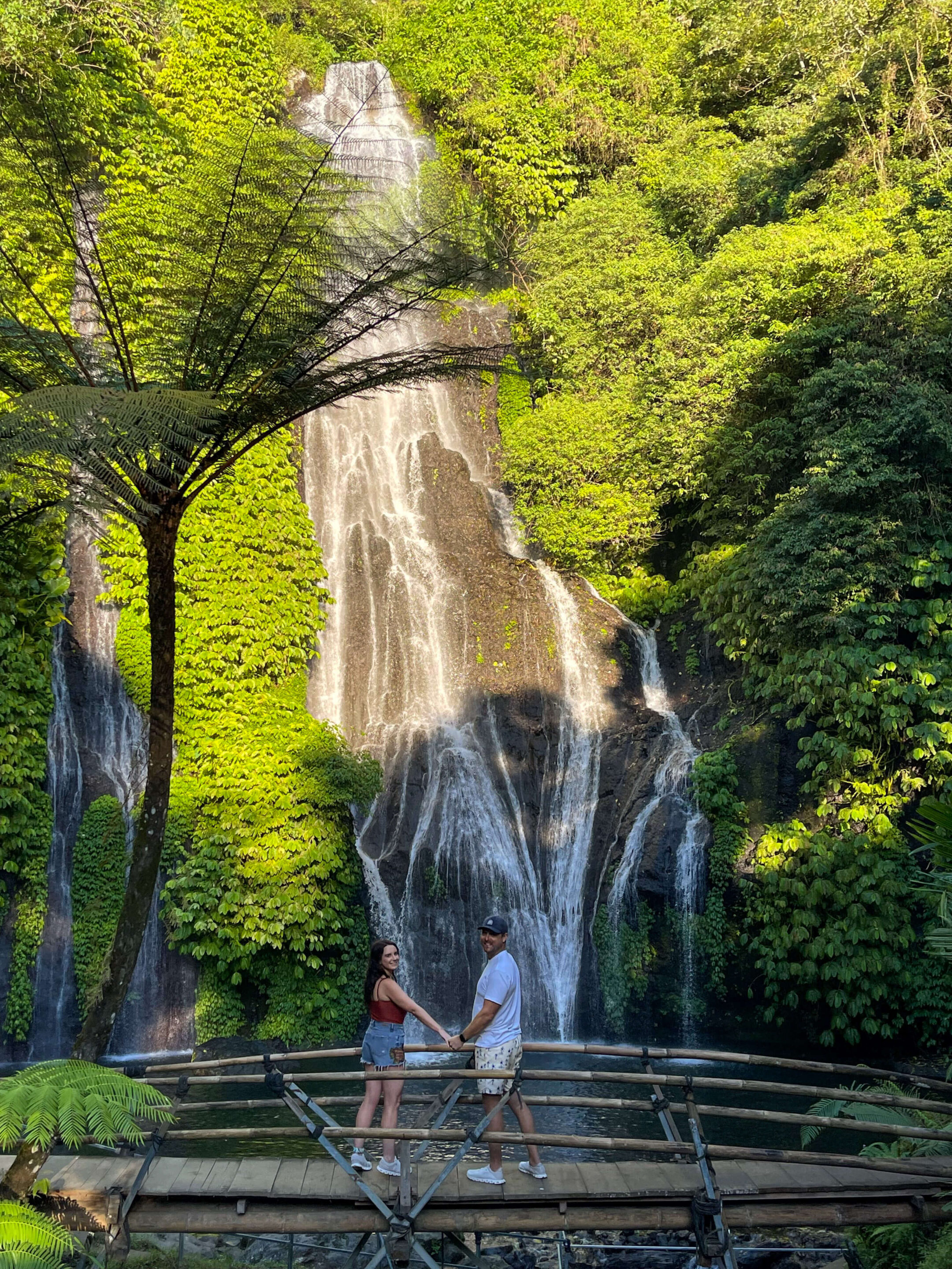 man and woman holding hands on a bridge overlooking Banyumala Twin waterfalls