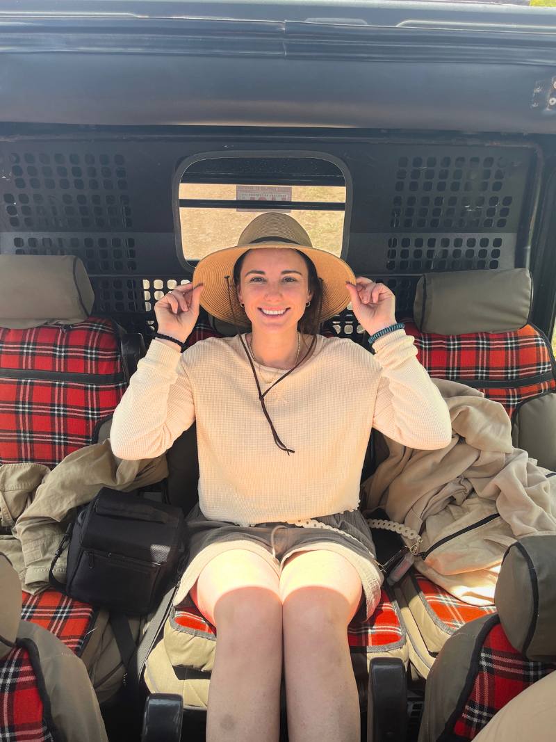 woman sitting in safari game drive vehicle holding on to the edge of her safari hat